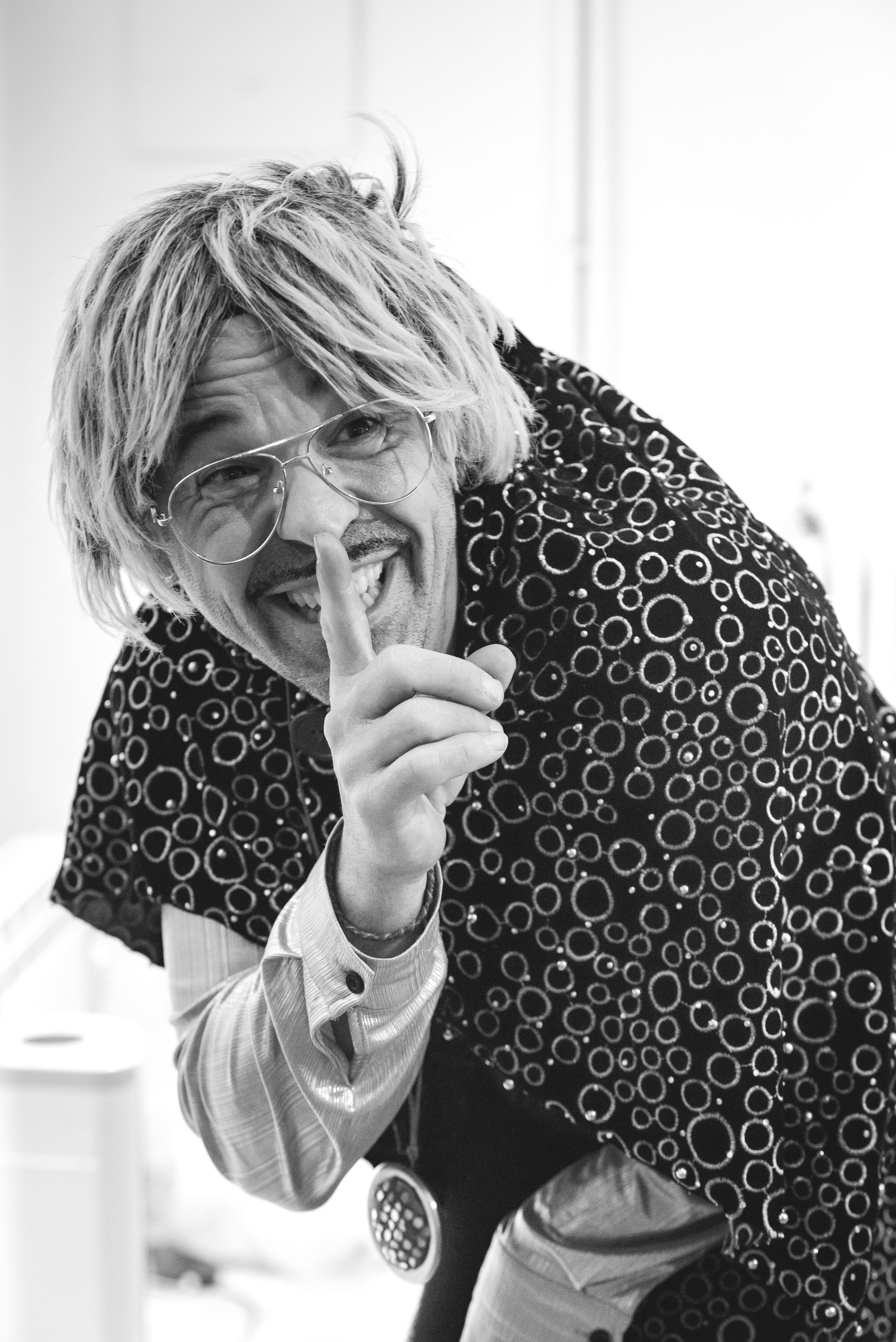 Retrato en blanco y negro de un actor haciendo el gesto de guardar silencio con una sonrisa pícara.