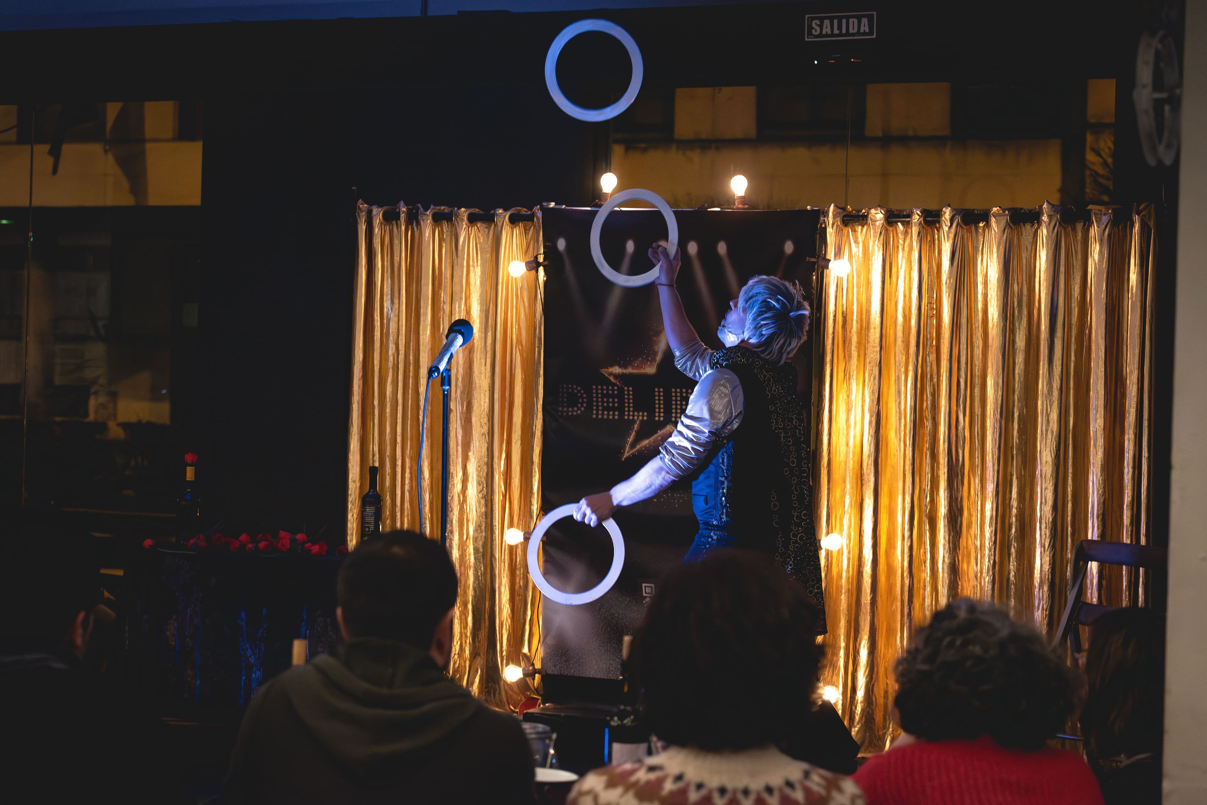 Artista de circo realizando malabares con aros luminosos frente al público con un telón dorado de fondo