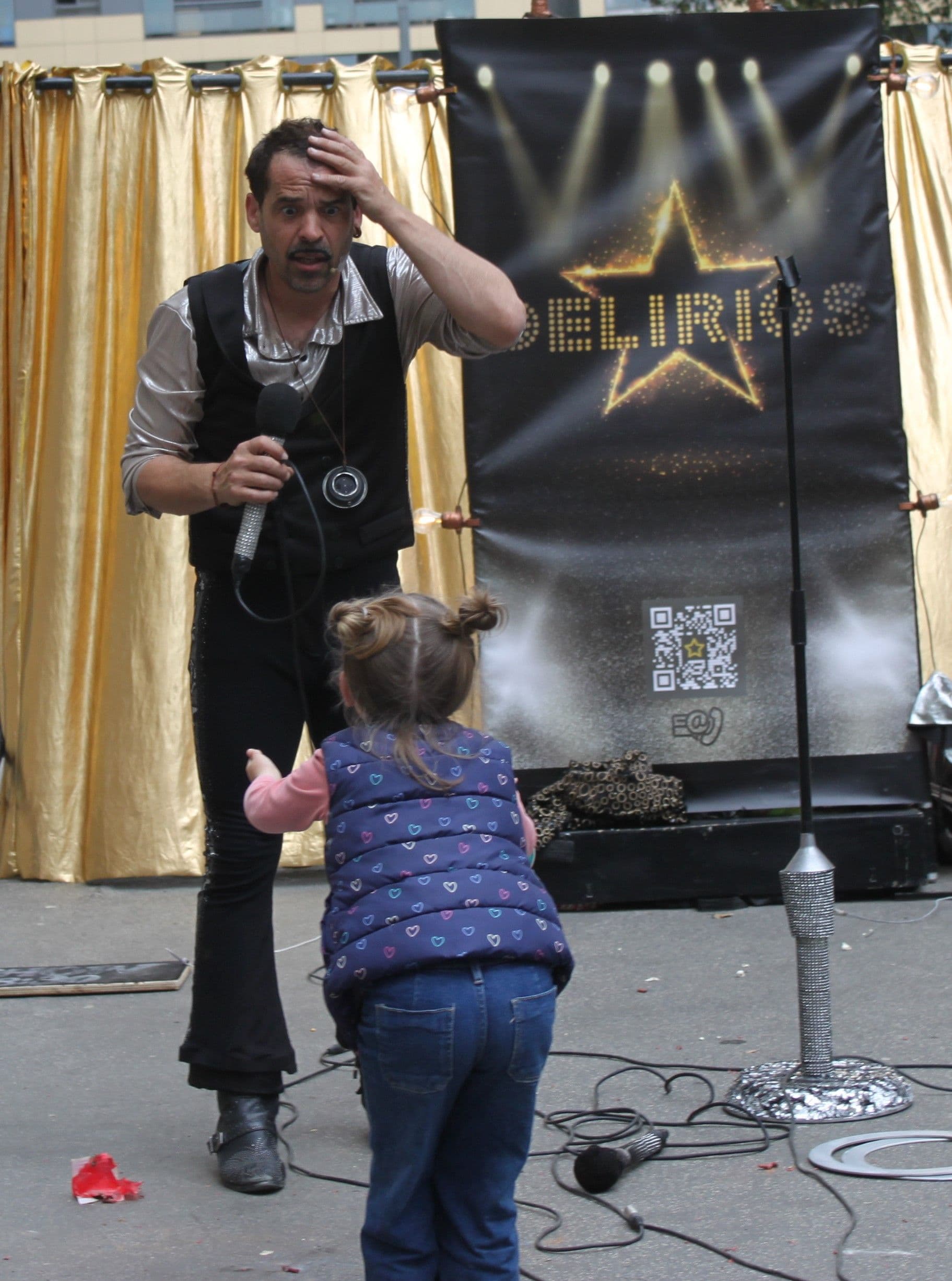 Actor con expresión de sorpresa interactuando con una niña del público durante un espectáculo callejero.