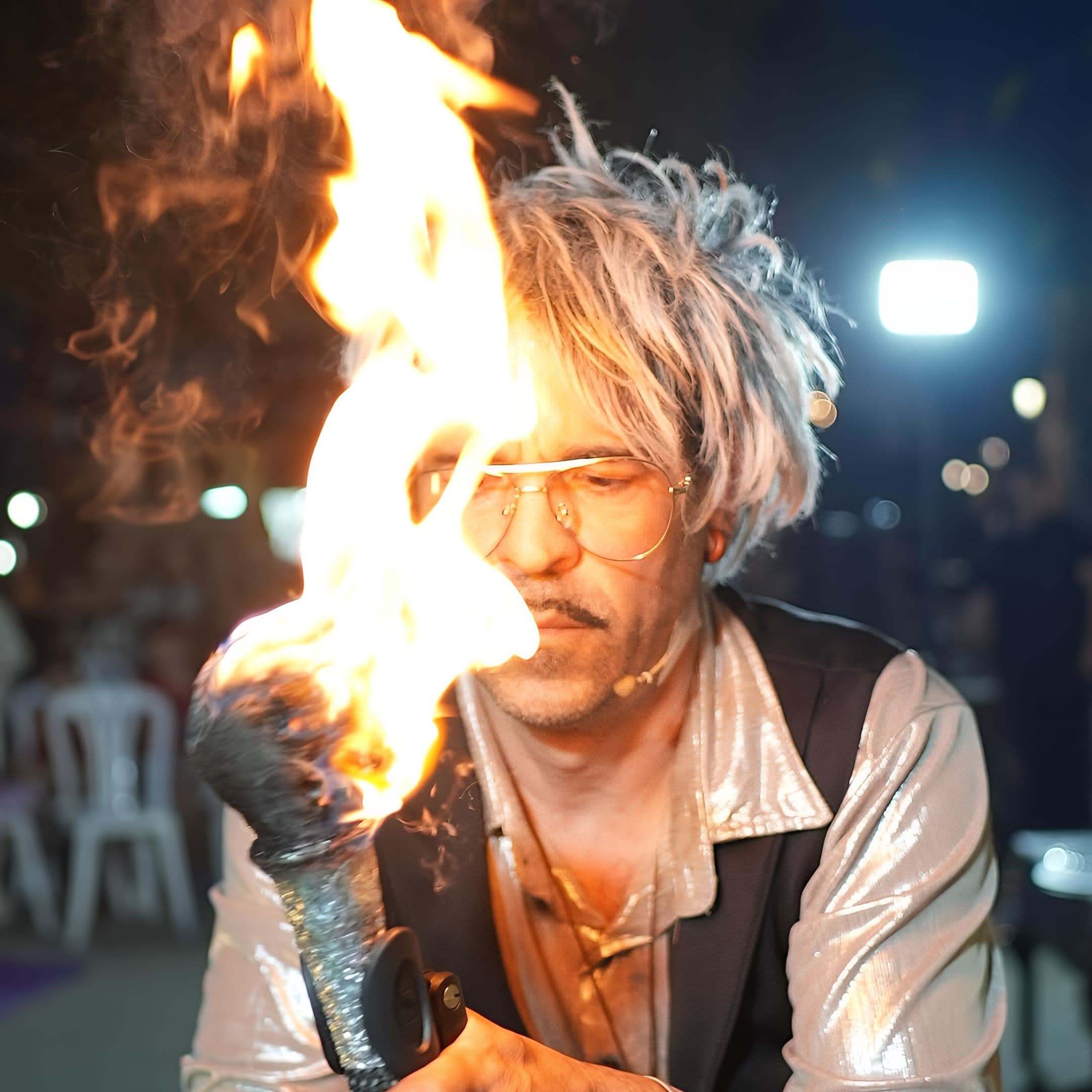 Actor iluminado por la llama de una antorcha que sostiene cerca de su rostro en un espectáculo nocturno.
